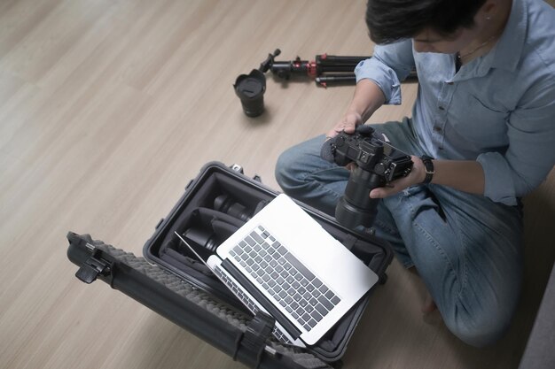 Профессиональный фотограф сидит на деревянном полу и регулирует камеру.