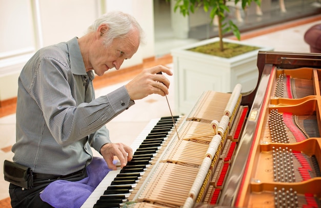 Professional piano technician repairing hammer mechanism using shank. Determined repairman trying to tune and restore vintage musical instrument keyboard.