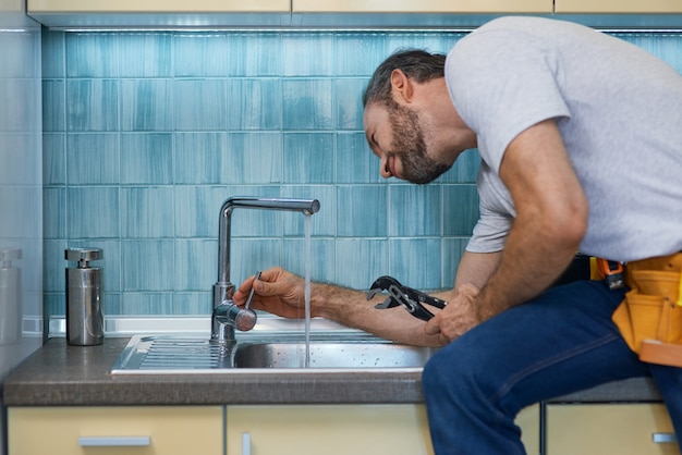 Professional plumber looking concentrated using pipe wrench while examining and fixing faucet in