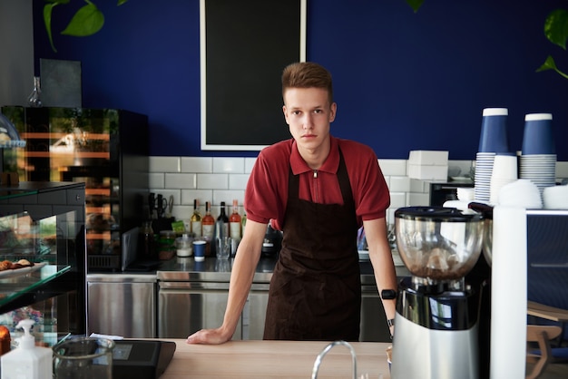 Professional portrait of young trained barista behind a bar counter in coffee shop. Small business, food and drink business concepts