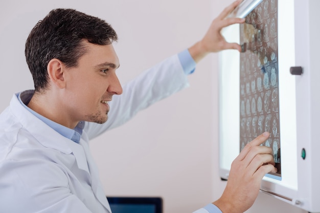 Professional radiologist. Positive hard working experienced man looking at the CT brain scan and smiling while noticing the improvement