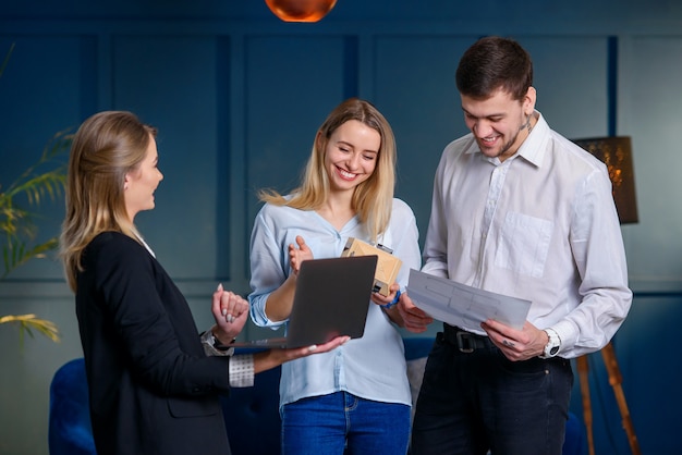 Professional realtor, designer showing plan of future design on the laptop to the couple of clients.