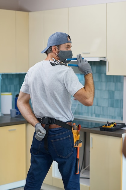 Professional repairman plumber wearing a mask posing with a pipe wrench while getting ready for