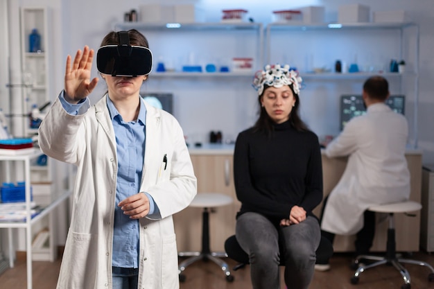 Professional researcher wearing virtual reality glasses using medical inovation in lab analysing brain scan of patient. Team of neurological doctors working with equipment high tech simulator device.