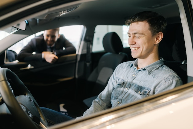 Professional sale assistant showing new car to customer in auto dealership