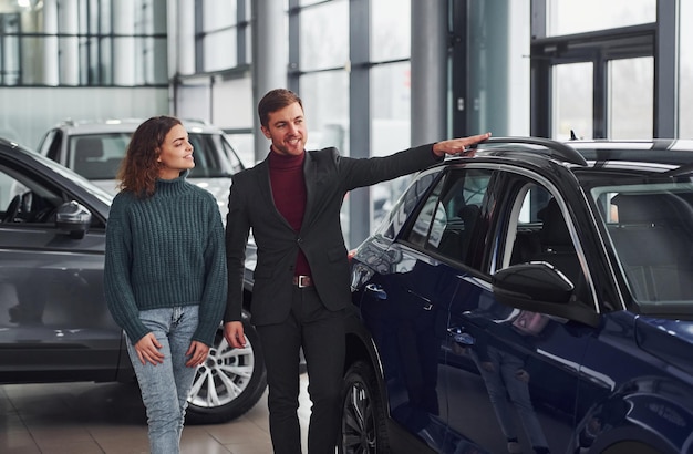 Venditore professionista che assiste la ragazza scegliendo la nuova automobile moderna all'interno.