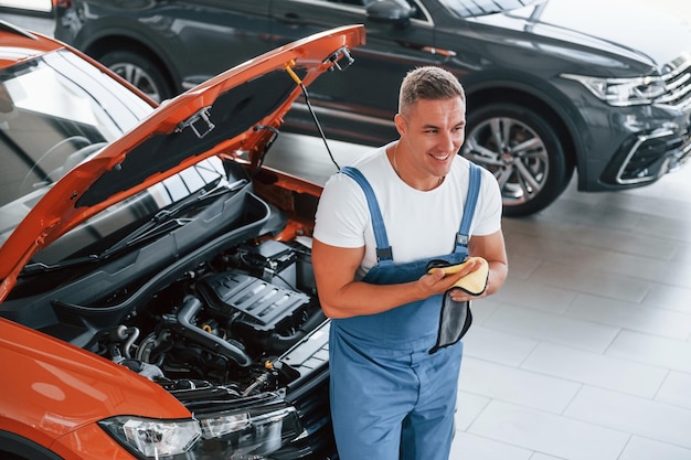 Professional service Man in uniform is repairing broken automobile indoors