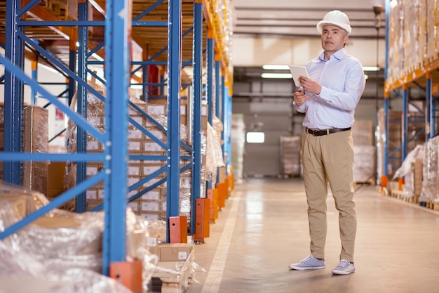 Professional skilled man using a tablet while doing the security check in the warehouse