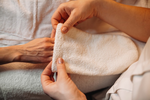 Professional spa worker is applying a special glove on the client's hand before starting the next spa procedure