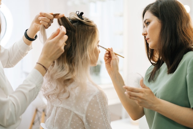 Professional stylist and makeup artist doing makeup and style hair for young woman