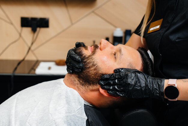 A professional stylist in a modern stylish barbershop shaves and cuts a young man's hair. Beauty salon, hair salon.