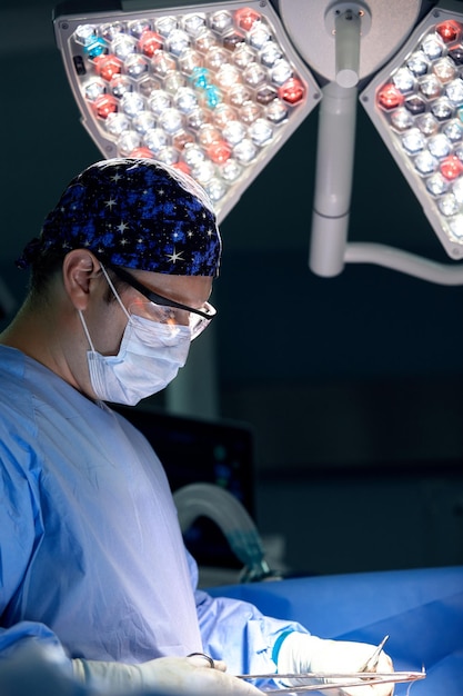 緊張したプロの外科医が手術室で傷を縫う現代の医療用ライトが彼を照らす男性外科医の控えめなコピースペース