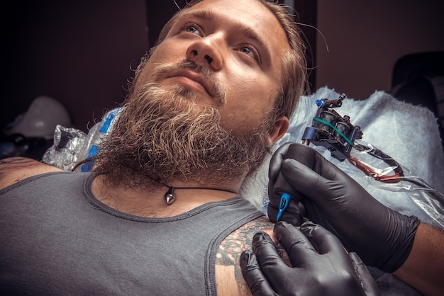 プロのタトゥーアーティストがタトゥーパーラーでタトゥーを作成します。/タトゥースタジオでポーズをとる手袋を着用した男性。