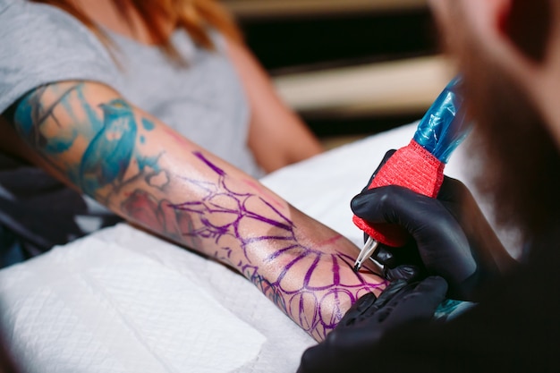 Профессиональный татуировщик делает татуировку на руке молодой девушки.