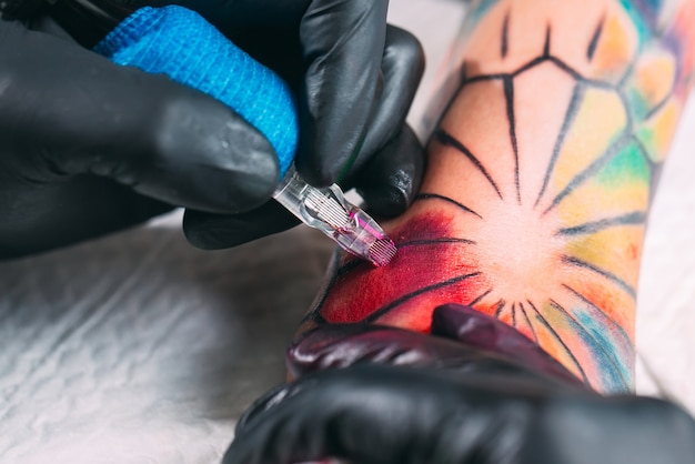 Профессиональный татуировщик делает татуировку на руке молодой девушки.