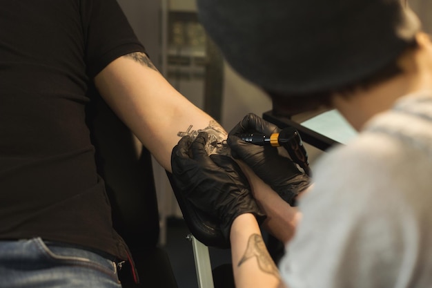 若い男の手に美しいタトゥーを作るプロのタトゥーアーティスト。特別な機械、コピースペースで男性の腕に絵を描く女性の彫師