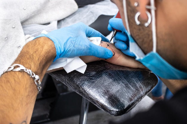 Профессиональный художник-татуировщик делает татуировку на руке Крупный план мужчины-татуировщика, делающего татуировку на руке клиенту