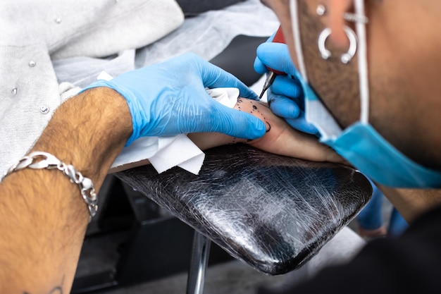 Professional tattoo artist making a tattoo on the hand Close up of male tattoo artist making a tattoo on the hand to client