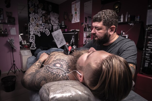 Foto tatuatore professionista che lavora alla mitragliatrice professionale in studio di tatuaggi. / il tatuatore fa un tatuaggio sulla pelle nel negozio di tatuaggi.