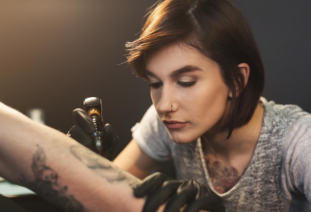 Photo a professional tattooer artist doing picture on man hand by machine. tattoo art on body. equipment for making black ink from a jartattoo art.