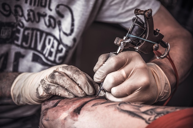 特別なツールのクローズアップによって手袋をはめてタトゥーを燃やすプロの刺青師。