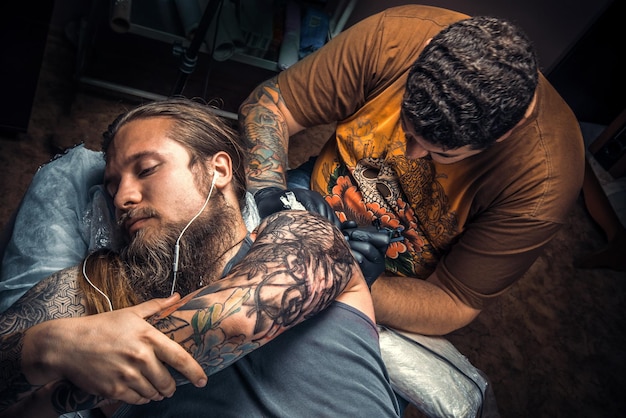 Professional tattooist posing in tattoo parlour./Professional tattooist makes cool tattoo in tattoo studio.