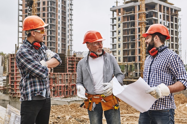 Professional team group of builders in protective wear and red helmets are discussing new project