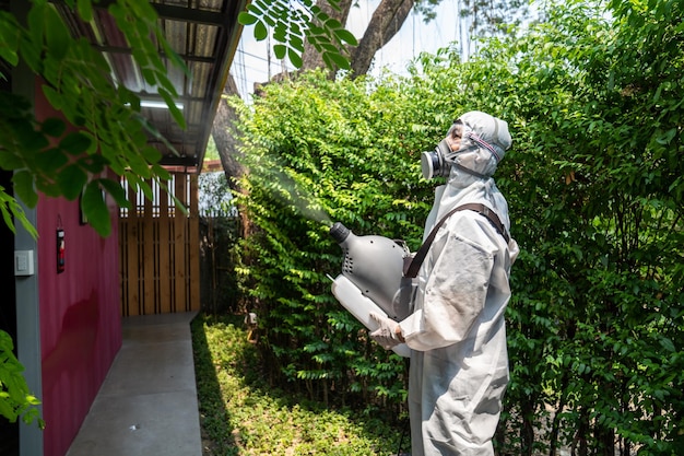 コロナウイルスCOVID19を浄化するために彼の滅菌機と屋外のフィールドで水スプレーを消毒することで予防スーツを着たプロの技術者