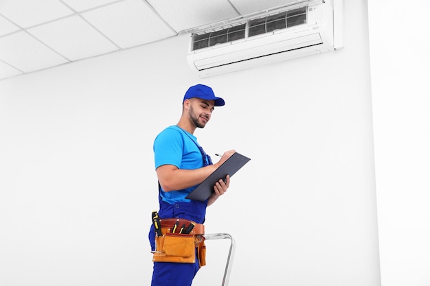 Photo professional technician with clipboard near modern air conditioner indoors