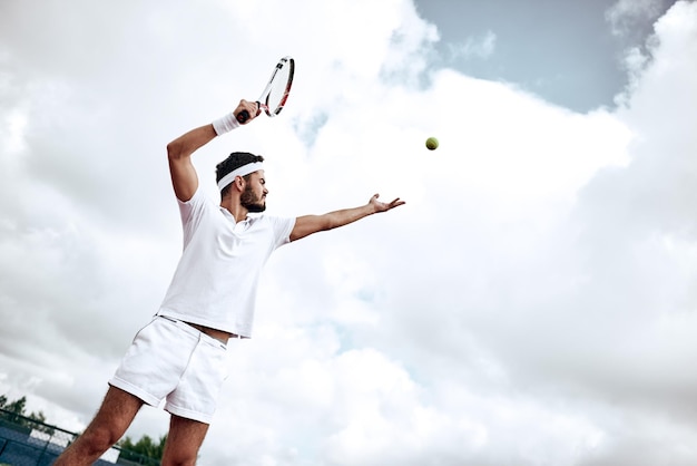写真 コートでテニスのゲームをしているプロのテニスプレーヤー。彼はラケットでボールを打つところです。ボールは宙に浮いています。