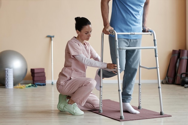 Professional therapist helping patient to walk using walker during rehabilitation in hospital