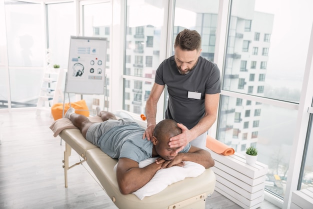 Professional therapist. Smart skilled man holding his patients head while working as a therapist in the rehabilitation center