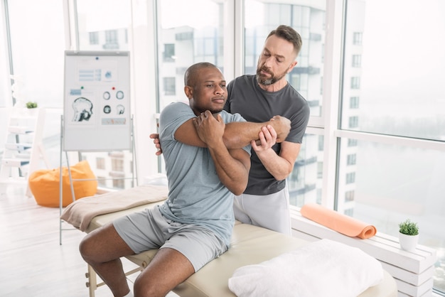 Professional therapy. Pleasant good looking man moving his body while being in the rehabilitation center