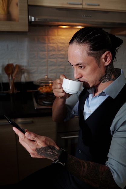 Commerciante professionista che beve una tazza di caffè mattutino e legge rapporti finanziari in movimento sul mercato sullo schermo dello smartphone