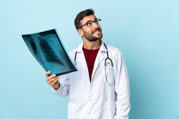 Professional traumatologist holding radiography isolated on blue background laughing and looking up