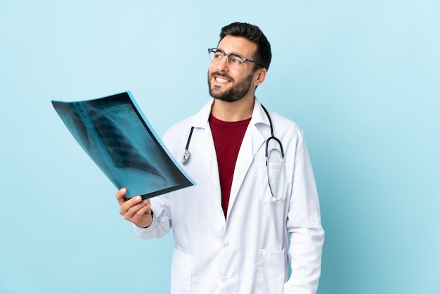 Professional traumatologist holding radiography isolated on blue wall laughing