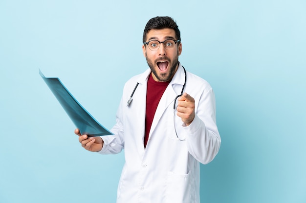 Professional traumatologist holding radiography isolated on blue wall points finger at you