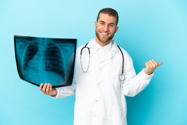 Professional traumatologist isolated on blue wall pointing to the side to present a product