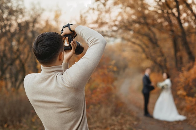 Photo professional wedding photographer taking pictures of the bride and groom in nature in autumn