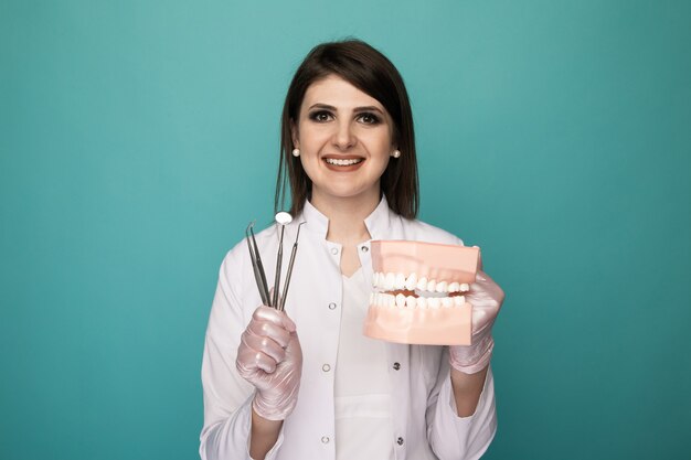 Professional woman dentist holding in hands jaw and instruments isolated in the blue studio.