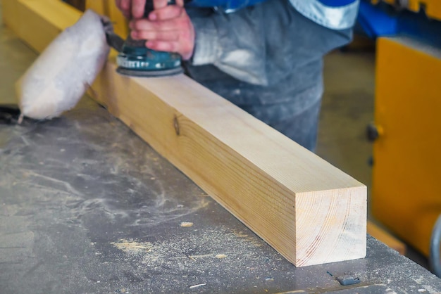 プロの木工職人がツールを使って大工ワーク ショップのワークベンチで木製の棒を挽く オーバーオールを着た中年労働者が電気グラインダーで木材を処理する 実際のワークフロー