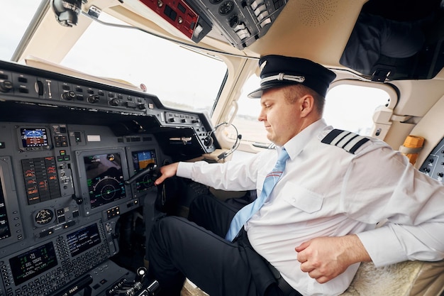 Professional worker Pilot in formal wear sits in the cockpit and controls airplane