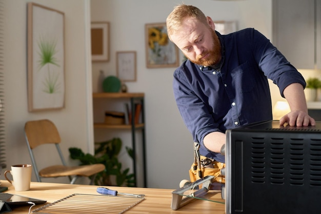 Professional worker repairing broken oven with tools in domestic kitchen