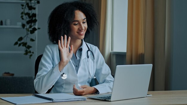 Professional young african lady doctor treat patient online in video chat on computer at hospital