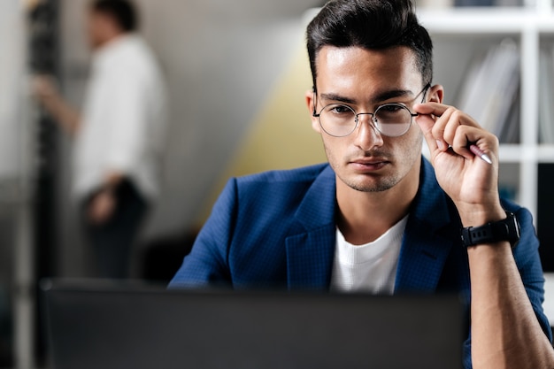 Professional young architect in glasses dressed in blue checkered jacket works on the laptop in the office .