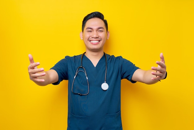 Photo professional young asian male doctor or nurse wearing a blue uniform giving a hug to a patient isolated on yellow background healthcare medicine concept