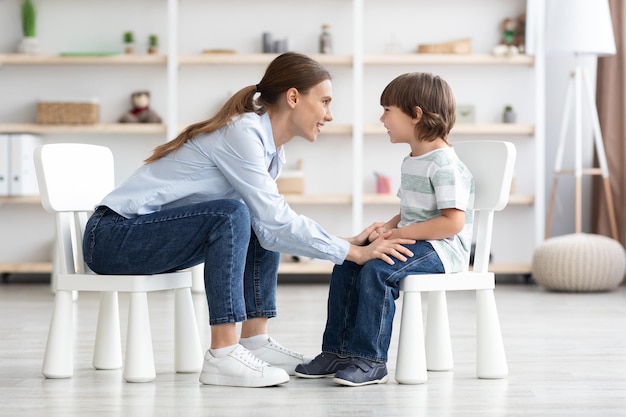 Professional young woman therapist communicating with happy little boy talking during personal