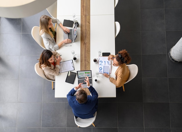 Professionals met een hoge hoek die bedrijfsrapporten analyseren, laptops en documenten op tafel in een vergadering