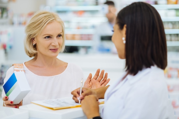 Professioneel advies. Vrolijke senior bezoeker die een glimlach op haar gezicht houdt terwijl ze met een internationale chemicus praat