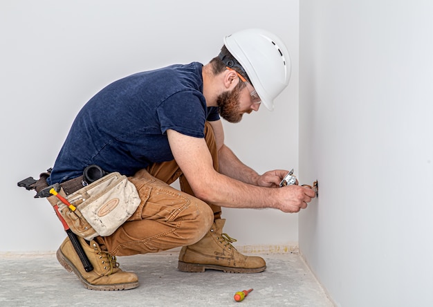 Professioneel in overall met een elektriciensgereedschap op de witte muurachtergrond. Huisreparatie en elektrisch installatieconcept.